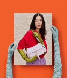 Model Liu Wen holding a white Prada handbag against an orange background with gloved hands holding a framed portrait.