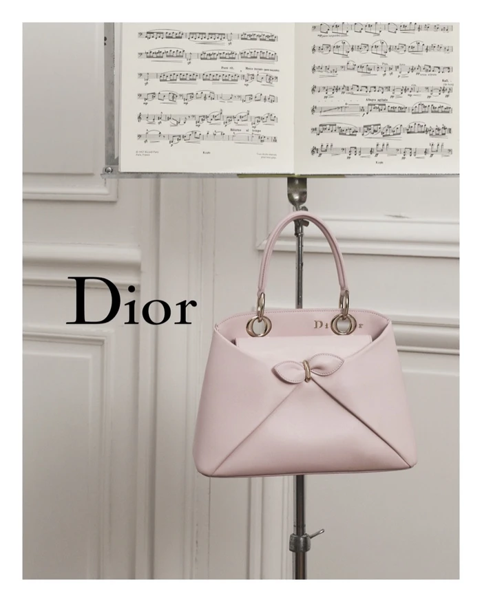 Pink Dior leather handbag displayed on a metal stand below an open sheet music stand in a room.