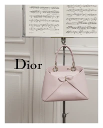 Pink Dior leather handbag displayed on a metal stand below an open sheet music stand in a room.