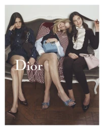 Three female models seated on a vintage grey sofa holding designer handbags for a Dior campaign