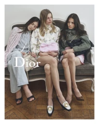 Three female models seated together on a velvet vintage sofa holding handbags for a Dior campaign photograph.