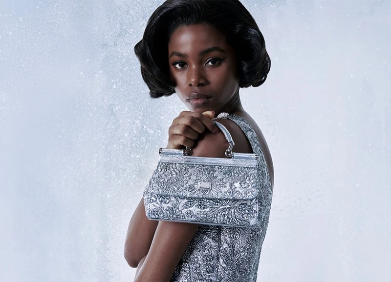 Model holding a metallic silver handbag against a pale textured background for Dolce and Gabbana Holiday 2025 campaign.