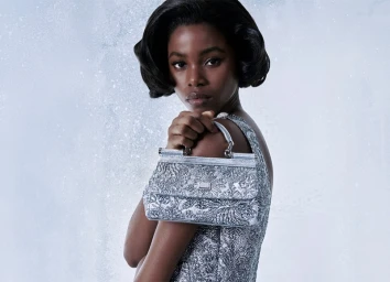 Model holding a metallic silver handbag against a pale textured background for Dolce and Gabbana Holiday 2025 campaign.