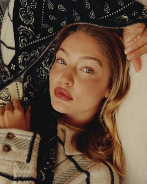 Gigi Hadid posing in a patterned black and white shawl with a cream jacket for Guest In Residence Winter 2025.