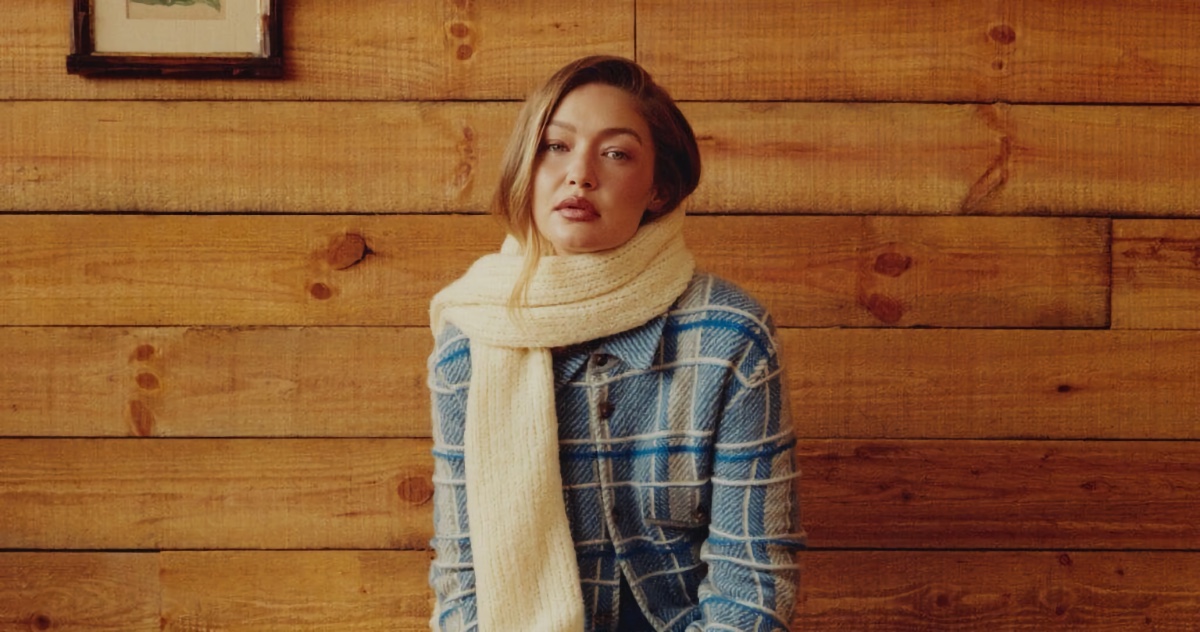 Gigi Hadid wearing a blue plaid shirt and cream knitted scarf against a wood paneled wall for Guest In Residence.