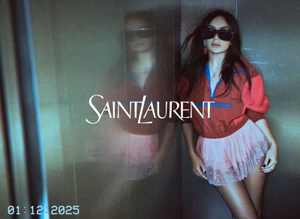 Model in dark sunglasses, red zip-up top, and pink lace miniskirt leaning against a reflective wall with a reflection