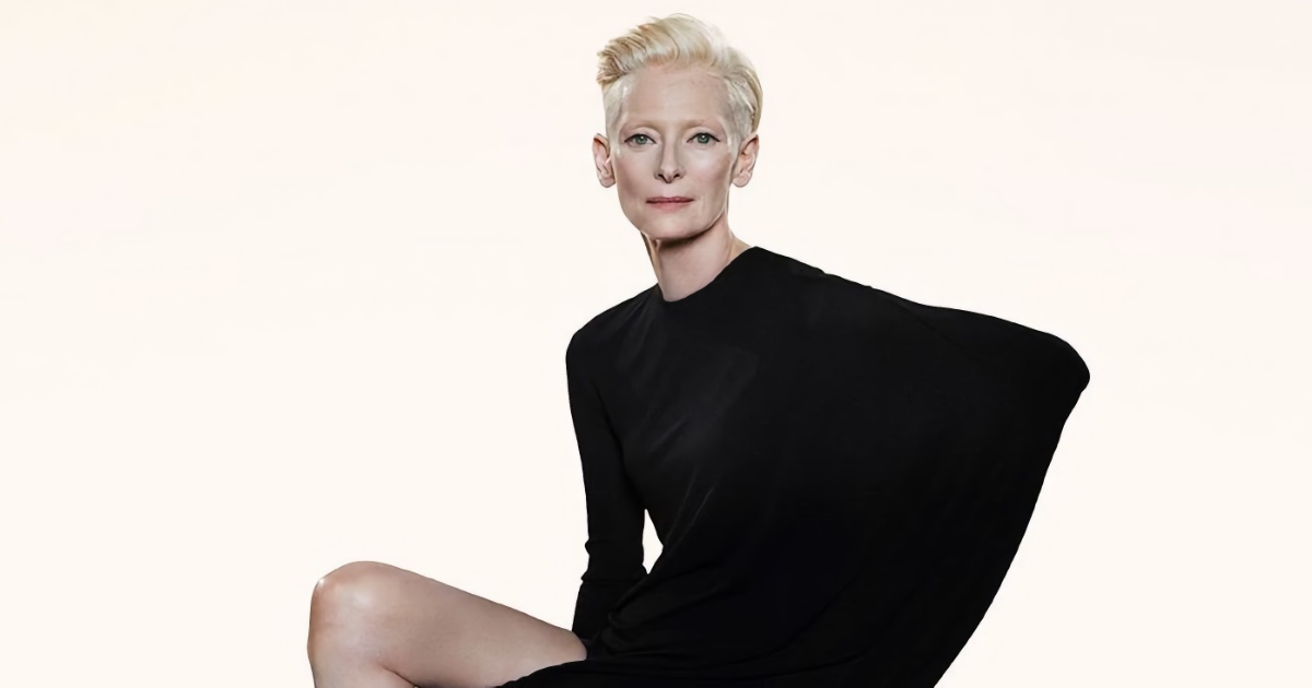 Tilda Swinton looking directly at camera, wearing a high-necked black structural dress against a stark white background.