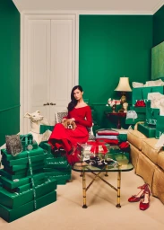 Woman in red dress holding a dog in a green room filled with J. Crew holiday shopping bags
