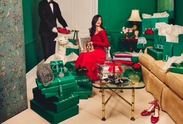 Woman in red dress holding a dog amid green J.Crew shopping boxes with a waiter holding a tray nearby