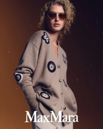 Model Dorit Revelis wearing a beige embroidered cardigan and sunglasses for Max Mara Holiday 2025