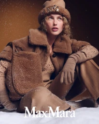 Model Dorit Revelis in a brown shearling coat and hat holding a bag in a snowy setting for Max Mara
