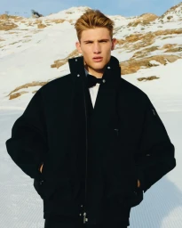 Model in black jacket and bow tie posing against a snowy mountain landscape