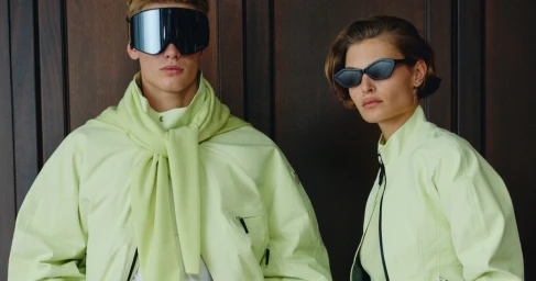 Man and woman wearing light green jackets and sunglasses against dark wooden paneling for Nike