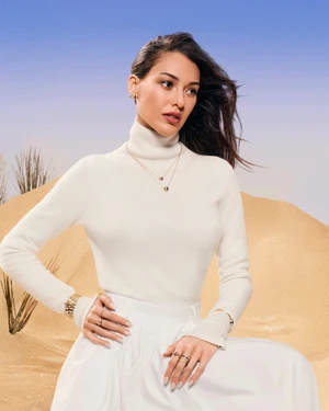 Woman wearing white turtleneck and jewellery posed against a sand dune backdrop for Boucheron Winter Wonderland 2025 campaign.
