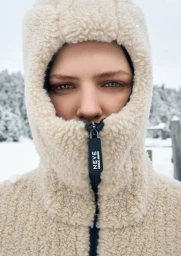 Model wearing a cream fleece hooded jacket with a black zipper pull in a snowy outdoor winter setting.