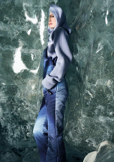 Model in a ribbed blue hooded sweater and matching trousers posing beside textured ice formations.