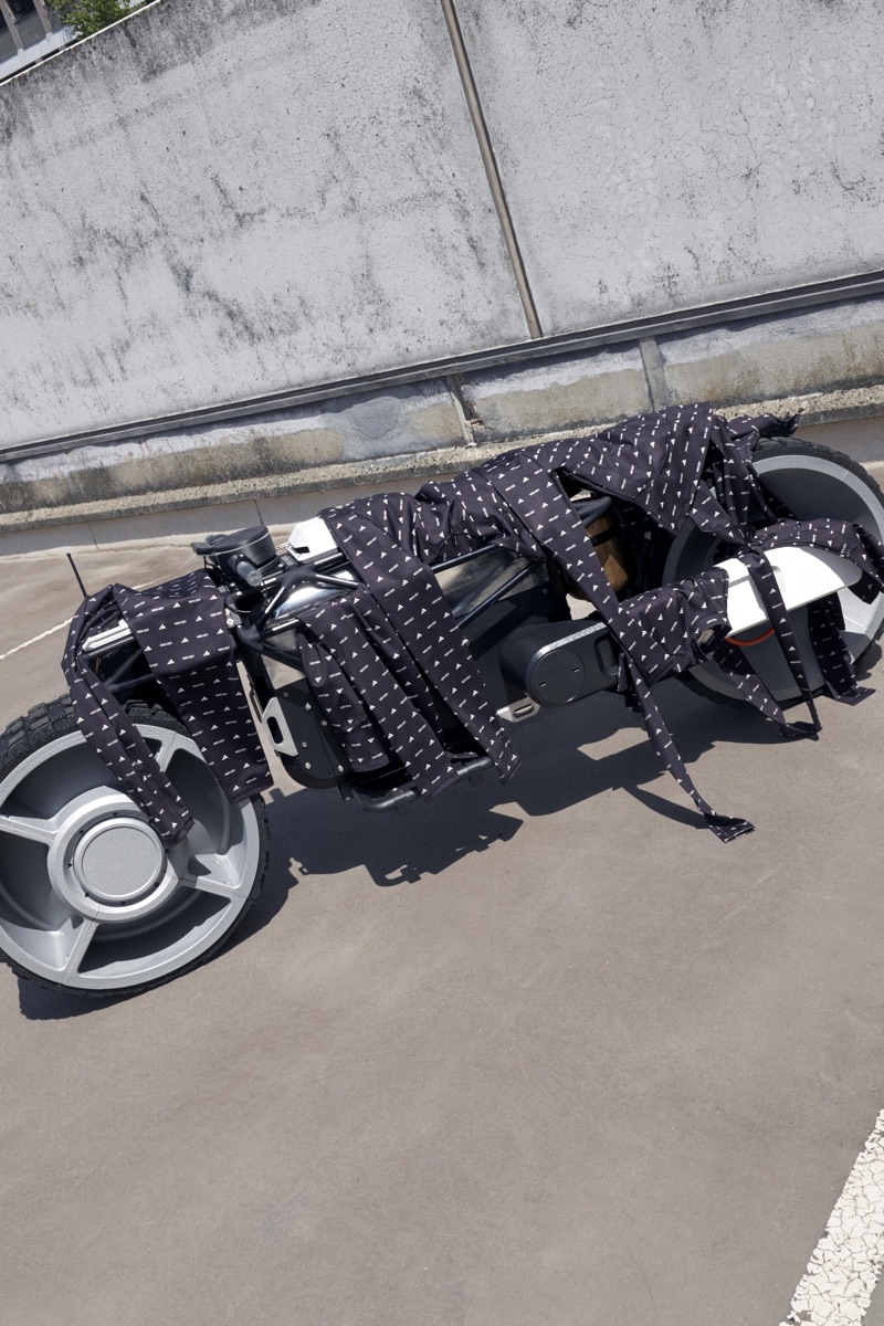 Futuristic motorcycle draped in patterned black fabric parked on asphalt against a concrete wall for Adidas Lunar Luxe Collab.
