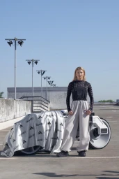 Frida Karlsson standing next to an Adidas concept vehicle on a concrete rooftop under a clear sky.