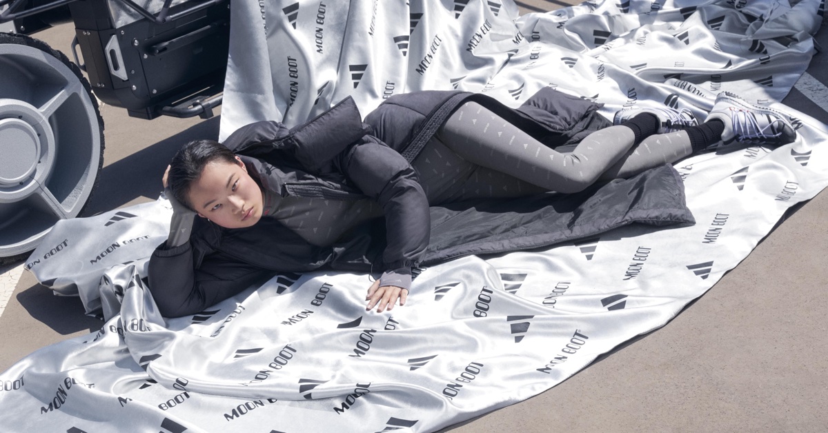 Model lying on a branded Moon Boot and Adidas blanket next to a wheel, wearing a dark puffer jacket and patterned leggings