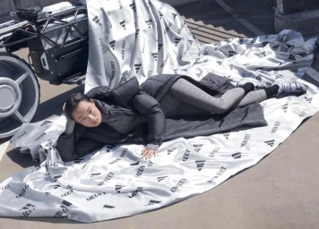 Model reclining on branded silver fabric next to a futuristic vehicle outdoors