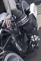 Close-up of a person wearing Adidas leggings and Moon Boot footwear seated on a futuristic vehicle