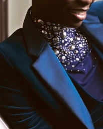 Close-up portrait of a person wearing a royal blue satin blazer and a high-neck top embellished with metallic silver studs and crystals.