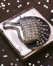 Silver rhinestone handbag resting on a vinyl record player surrounded by scattered sequins on a dark textured surface.