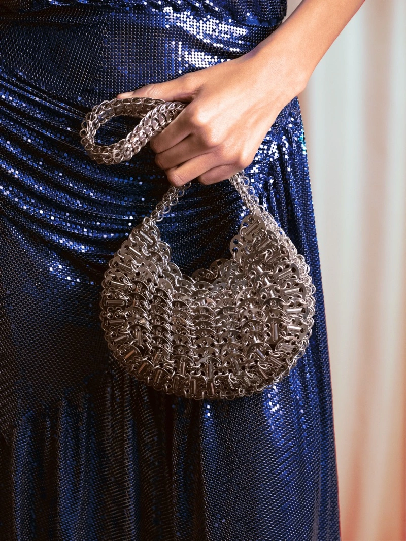 Close-up of a person holding a metallic chainmail handbag against a glittering blue sequin dress for Rabanne Resort 2026 Party.