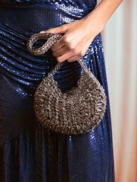 Close-up of a person holding a metallic chainmail handbag against a glittering blue sequin dress for Rabanne Resort 2026 Party.