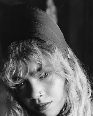 Close-up portrait of a model with wavy hair and a nose ring wearing a structured cap for Louis Vuitton Cruise 2026