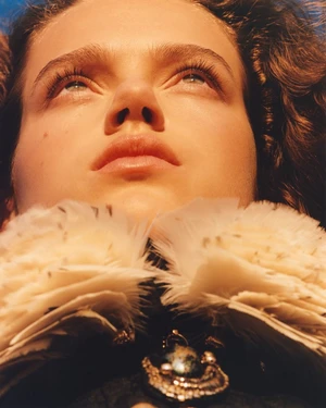 Close up portrait of a model looking upward wearing a textured white feather collar and dark pendant necklace