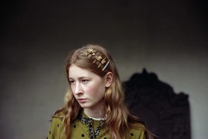 Close-up portrait of a woman with long wavy hair wearing decorative gold hair clips and an olive green embellished cardigan.