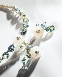 Close-up of Giorgio Armani gemstone necklace and earrings featuring blue and green stones with white flower motifs on white surface