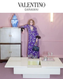 Marisa Berenson in a purple patterned dress with fur cuffs leaning against a cabinet in a pink room for Valentino Notturno