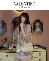 Dakota Johnson holding a cream handbag in an ornate room with framed portraits for Valentino Notturno