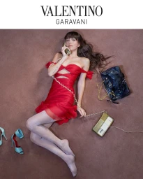Dakota Johnson in a red dress lying on a carpeted floor holding a telephone for Valentino Notturno campaign