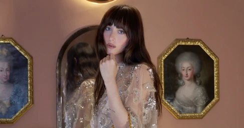 Dakota Johnson in embellished sheer dress posing against warm wall with framed classical portraits for Valentino Notturno