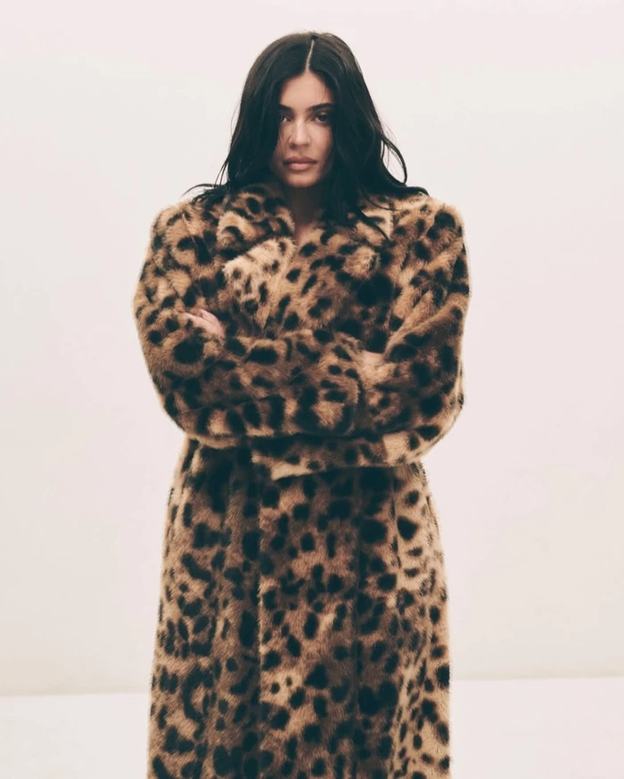 Kylie Jenner wearing a leopard print faux fur coat with arms crossed against a plain white background