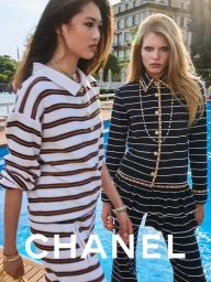 Two models wearing striped Chanel clothing standing near an outdoor swimming pool by a waterfront resort