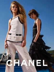 Two female models posing outdoors against a clear blue sky, wearing Chanel knitwear and holding a chain handbag.