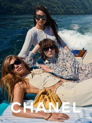Three models wearing sunglasses on a boat on the water for the Chanel Cruise 2026 campaign.
