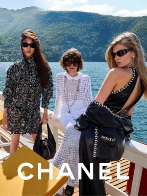 Three female models wearing designer fashion and sunglasses posing by a lake with mountains in the background for Chanel.