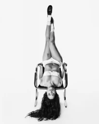 Rosalia hanging upside down over a chair in underwear and socks against a white studio background for Calvin Klein.