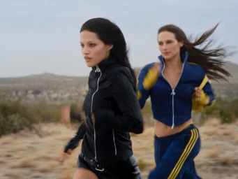 Two women running outdoors through a desert landscape wearing matching zip-up track jackets by Adidas