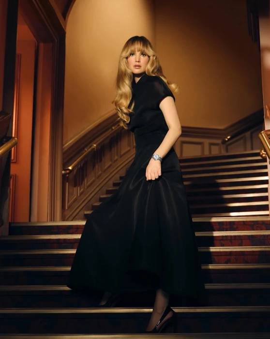 Jennifer Lawrence wearing a black dress and watch standing on grand staircase