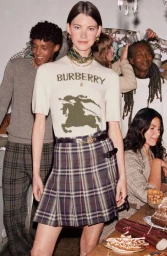 Model in cream Burberry knit top and plaid skirt standing before a group at a holiday table set by Angelo Pennetta.