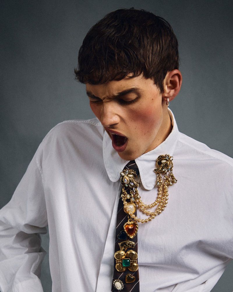 Young adult male in a white dress shirt with a decorated tie, open mouth, looking down against a gray background in a studio shot.