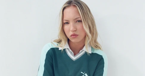 Lila Moss wearing a green and white V-neck pullover against a plain white background for Puma