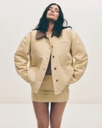 Kylie Jenner wearing a beige canvas jacket and matching miniskirt against a plain white studio background.