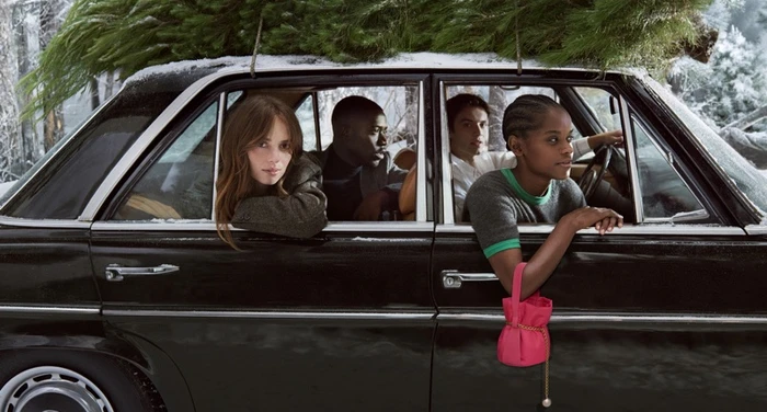 Maya Hawke, Damson Idris, Louis Partridge, and Letitia Wright inside a black vintage car with a Christmas tree strapped to the roof.
